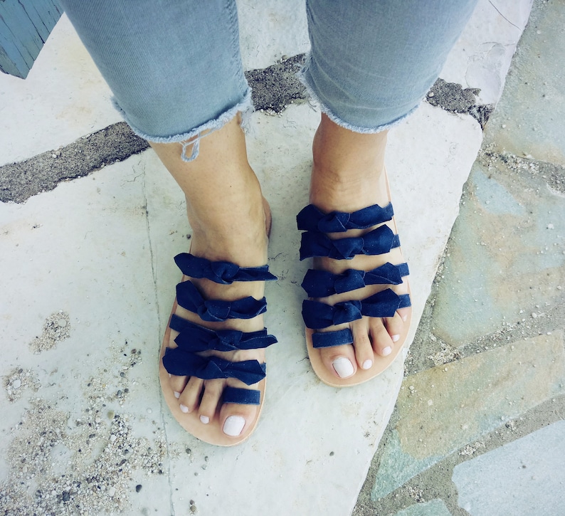 May include: A pair of blue sandals with multiple navy blue bows across the straps. The sandals are worn on a person's feet.