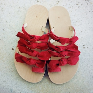 May include: A pair of sandals with red bows. The sandals are made of leather and have a flat sole.
