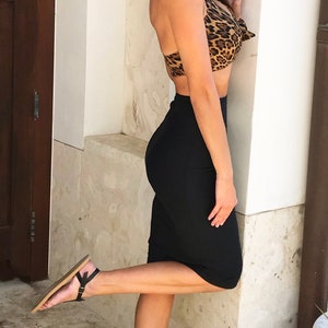 A woman wearing a black skirt and a leopard print halter top. She is standing with one leg raised and is wearing black sandals.