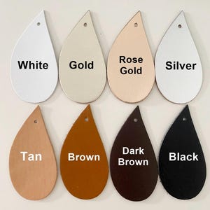 Op de afbeelding: Acht druppelvormige lederen oorbelblanco's gerangschikt in twee rijen. De bovenste rij bevat de kleuren wit, goud, ros&eacute;goud en zilver. De onderste rij toont de kleuren tan, bruin, donkerbruin en zwart. Elk stuk heeft een gaatje aan de bovenkant.