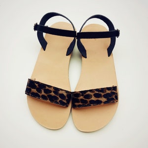 May include: A pair of brown leather sandals with black straps and a leopard print detail on the front.