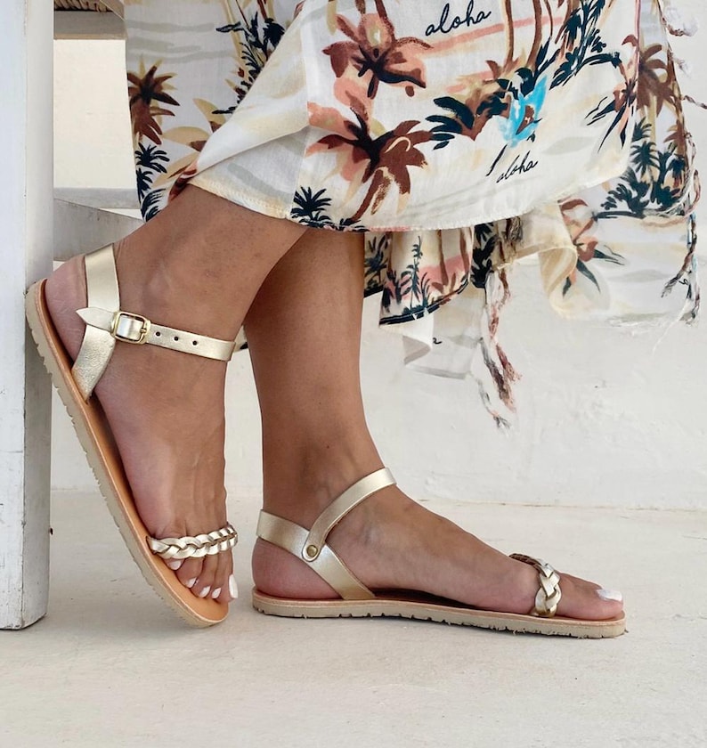 Model wearing gold handcrafted leather barefoot sandals with a thin Vibram sole and braided strap detail, styled with a summer dress.