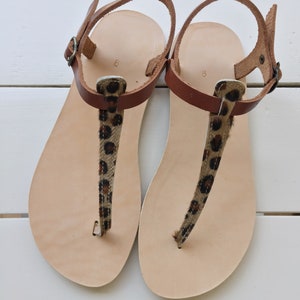 A pair of brown leather sandals with leopard print straps. The sandals have a simple design and are perfect for summer.
