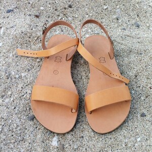 May include: A pair of tan leather sandals with adjustable straps. The sandals have a simple design and are perfect for summer.