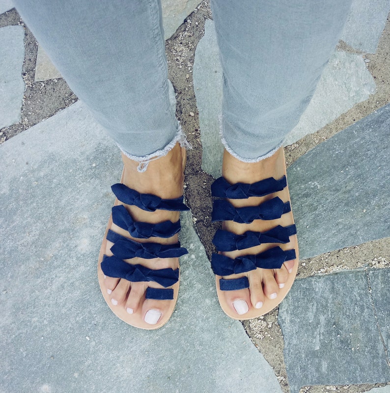May include: A pair of blue sandals with multiple navy blue bows on each strap. The sandals are worn on a person's feet, with the toes visible.