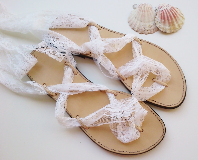 May include: A pair of white leather sandals with lace straps. The sandals are tied around the ankles and have a simple design.