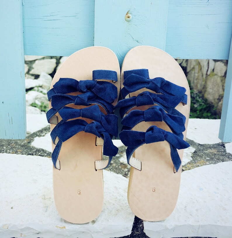 May include: A pair of leather sandals with blue ribbon straps. The sandals have a simple design and are perfect for summer.