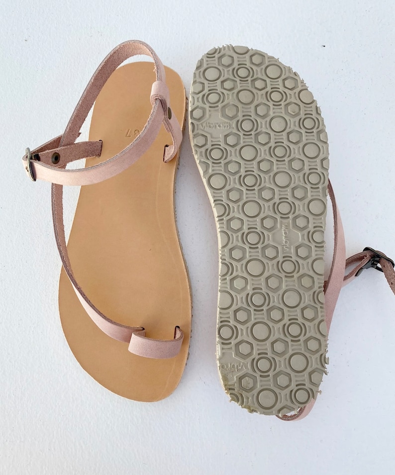 Peut inclure: Une paire de sandales en cuir rose clair avec une semelle en cuir marron. Les sandales ont une seule sangle qui passe autour de la cheville et une boucle d'orteil. La semelle a un motif textur&eacute;.