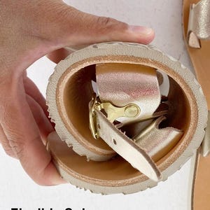 Hand bending a black leather T-strap sandal to demonstrate the extreme flexibility of the barefoot sole for natural foot movement.