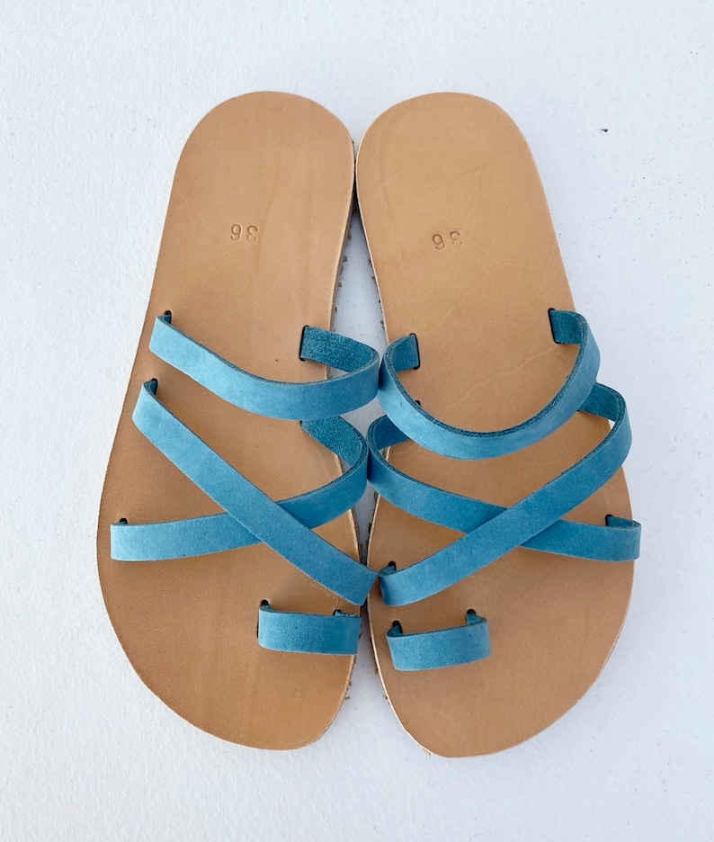 "Top-down view of a pair of handmade natural leather sandals on a neutral background, showing the anatomical shape and quality craftsmanship.