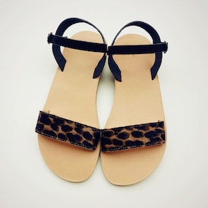 Peut inclure: Une paire de sandales plates dot&eacute;es d'une semelle int&eacute;rieure beige et d'une bride avant unique avec un motif l&eacute;opard marron et noir. Chaque sandale comprend une fine bride de cheville noire avec une petite boucle en m&eacute;tal pour le maintien.
