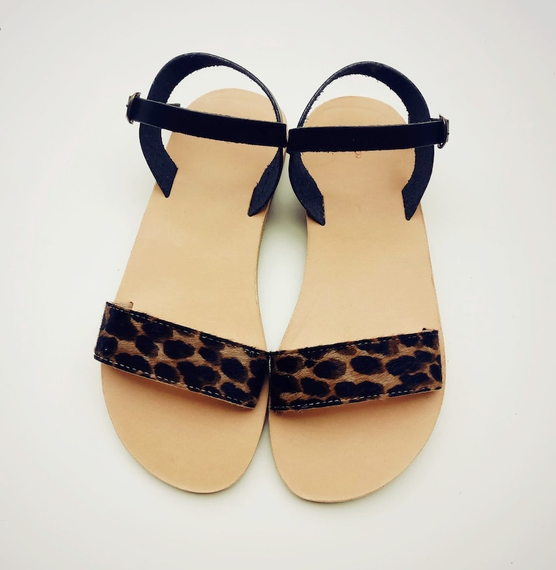 Peut inclure: Une paire de sandales plates dot&eacute;es d'une semelle int&eacute;rieure beige et d'une bride avant unique avec un motif l&eacute;opard marron et noir. Chaque sandale comprend une fine bride de cheville noire avec une petite boucle en m&eacute;tal pour le maintien.