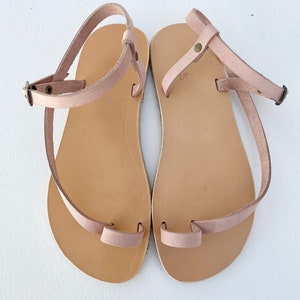 Peut inclure: Une paire de sandales en cuir marron clair avec une boucle d'orteil et une sangle de cheville. Les sandales ont un design simple et sont parfaites pour les beaux jours.