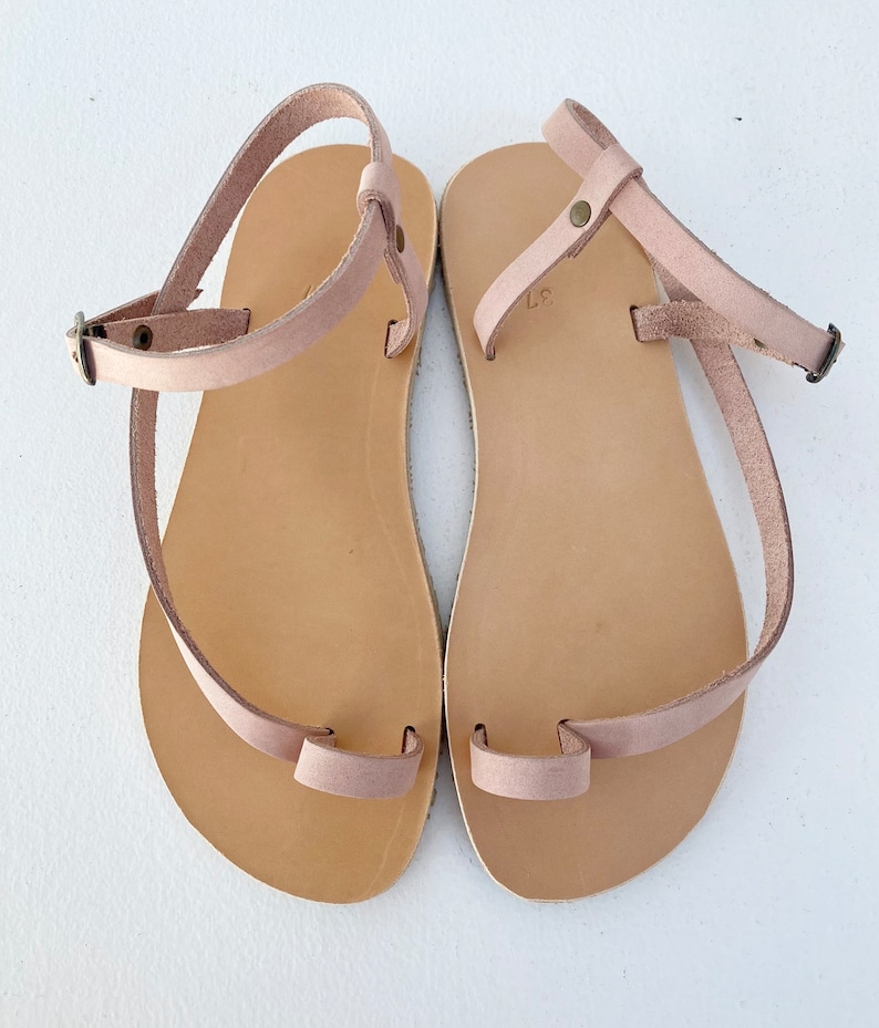 Peut inclure: Une paire de sandales en cuir marron clair avec une boucle d'orteil et une sangle de cheville. Les sandales ont un design simple et sont parfaites pour les beaux jours.