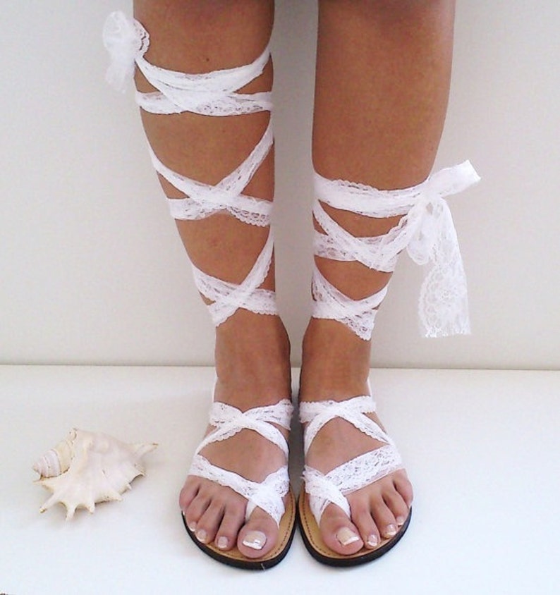 May include: White lace sandals with straps that wrap around the ankles and legs. The sandals have a simple design and are perfect for a beach wedding or other special occasion.