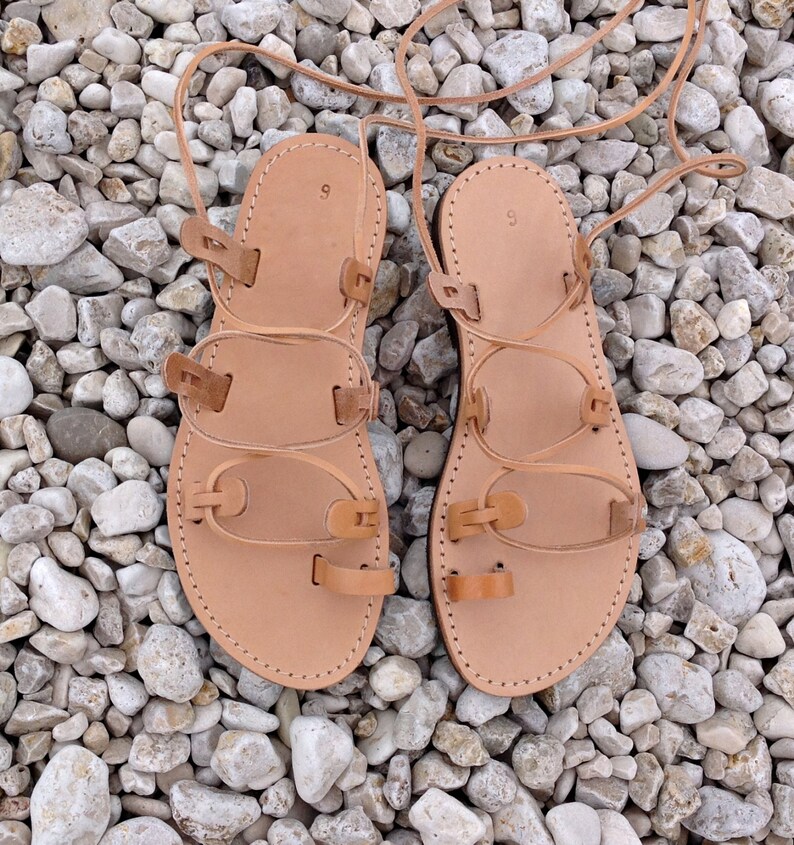 Op de afbeelding: Een paar beige leren gladiatorsandalen met een teenlus, meerdere horizontale bandjes en lange veters om rond de enkel te wikkelen. Op het voetbed van elke sandaal staat het cijfer 9 gestempeld, wat de schoenmaat aangeeft.