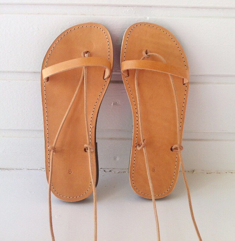 May include: A pair of tan leather sandals with laces that tie up the legs. The sandals have a simple design and are made of high-quality leather.