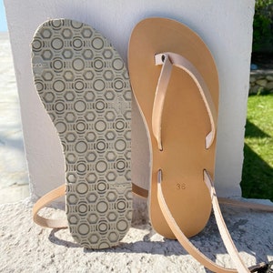 May include: A pair of tan leather thong sandals with a simple design. The sandals have a textured sole and a size 36 label.