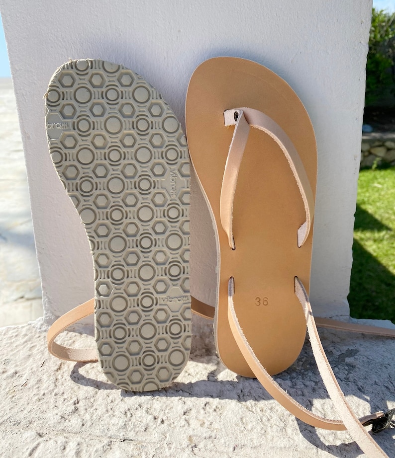 May include: A pair of tan leather thong sandals with a simple design. The sandals have a textured sole and a size 36 label.