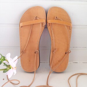 May include: A pair of tan leather sandals with laces that tie up the legs. The sandals have a simple design with a single strap across the top of the foot.