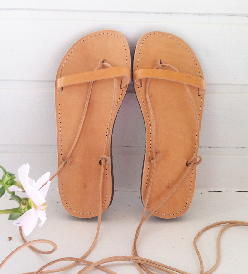 May include: A pair of tan leather sandals with laces that tie up the legs. The sandals have a simple design with a single strap across the top of the foot.