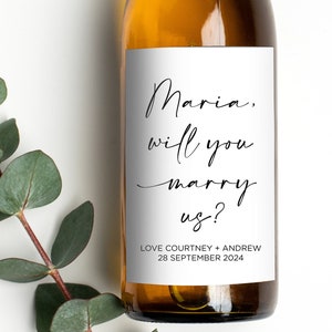 May include: A white wine bottle with a white label that says "Maria, will you marry us?" Love Courtney + Andrew 28 September 2024.