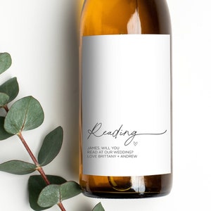 May include: A white wine bottle with a label that says "Reading" in cursive with a heart symbol. The label also says "James, will you read at our wedding? Love Brittany + Andrew".