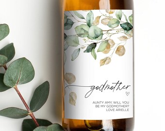 May include: A white wine bottle with a green and gold floral design label. The label says "godmother" with the text "Aunty Amy will you be my godmother? Love Arielle".