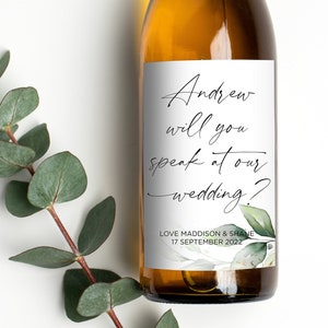May include: A white wine bottle with a label that says "Andrew will you speak at our wedding?" with a green floral design. The label also includes the names "Love Maddison & Shane" and the date "17 September 2022".