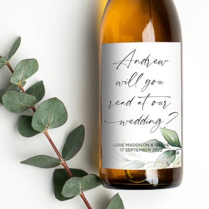 May include: A white wine bottle with a personalised label that reads "Andrew will you read at our wedding?" with a floral design and the date "17 September 2022".