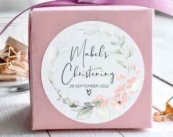 May include: A pink gift box with a light purple ribbon tied around it. The box has a round sticker with a floral design and the text "Mabel's Christening 28 SEPTEMBER 2022".