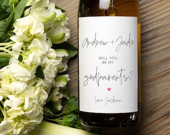 May include: A white wine bottle with a personalized label that says "Andrew + Jade Will you be my godparents? Love Jackson". The label has a pink heart.