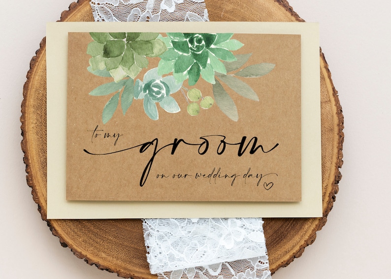 May include: A kraft paper card with a watercolor illustration of succulents and the text "to my groom on our wedding day" with a small heart.
