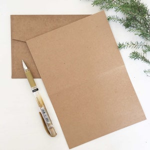 May include: A brown card with a brown envelope and a gold pen on a white surface.