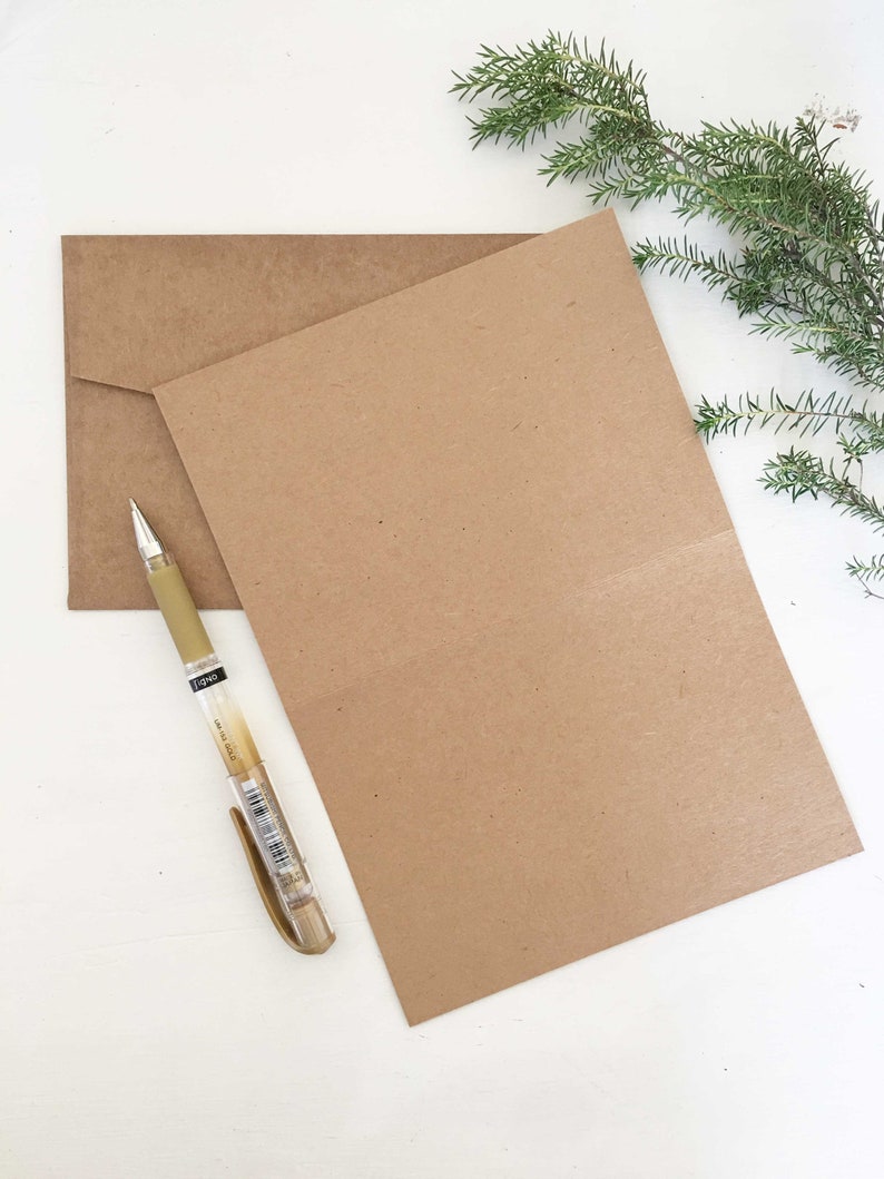 May include: A brown card with a brown envelope and a gold pen on a white surface.