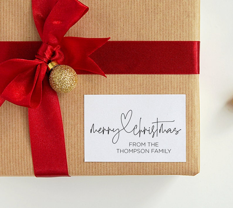 May include: A brown gift box with a red ribbon and a gold ornament. A white gift tag with black text reads "merry christmas from the Thompson family".