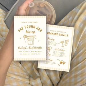 May include: Two rectangular bachelorette party invitation cards with a cream background and light yellow vertical stripes. The text reads "She Found Her Honey" and "Audrey's Bachelorette Weekend Details" with illustrations of a honey jar, cocktails, and heart-shaped sunglasses in gold ink.