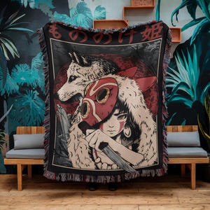 Puede incluir: Una manta tejida con una ilustración detallada de un lobo y un personaje con una máscara roja. El diseño incluye texto japonés en la parte superior y un borde negro con flecos. La paleta de colores incluye rojo, negro, blanco y beige.