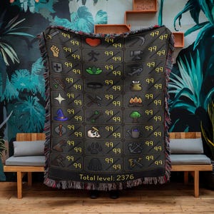 May include: A dark gray woven blanket featuring a grid of icons and the number 99. The blanket has a black fringe and the text "Total level: 2376" at the bottom. The icons are in various colors and represent different skills.