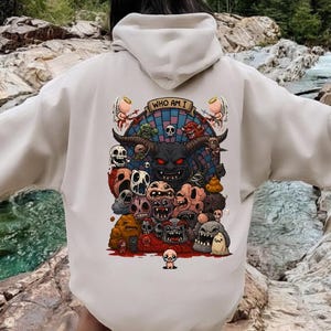 May include: Beige hoodie with a graphic illustration on the back. The illustration features a demonic figure with horns, surrounded by various monster-like characters and the text "WHO AM I".