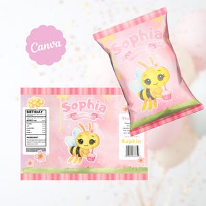 Puede incluir: Bolsa de patatas fritas y etiqueta rosas con temática de cumpleaños, con una abeja de dibujos animados sosteniendo una magdalena. La bolsa y la etiqueta tienen el nombre "Sophia" en una fuente decorativa. La etiqueta incluye una sección de información nutricional y la palabra "Cumpleaños".