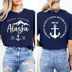 Puede incluir: Camiseta azul marino con texto y gr&aacute;ficos blancos. La parte delantera de la camiseta dice "Cruisin' Together Alaska 2026" con un dise&ntilde;o de monta&ntilde;a y ancla. La parte trasera de la camiseta tiene un dise&ntilde;o circular con el nombre "Irene" y un ancla.