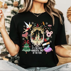 May include: Black t-shirt with a colorful holiday graphic. The design includes a castle, fairy, Christmas tree, and the text "It's the Most Wonderful Time of the Year". Festive elements like candy and snowflakes are also present.