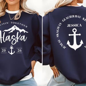 Puede incluir: Sudadera azul marino con texto y gr&aacute;ficos blancos. La parte delantera presenta "Cruisin' Together Alaska" con un gr&aacute;fico de monta&ntilde;a, ancla y el a&ntilde;o "2026". La parte trasera tiene un dise&ntilde;o circular con "Glacier Bay, Ketchikan, Victoria, Juneau, Skagway" y un ancla.