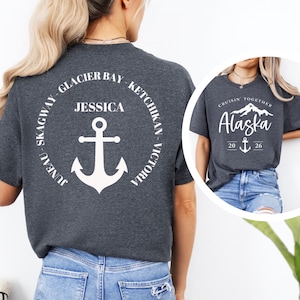 Puede incluir: Camisetas grises oscuras con dise&ntilde;os gr&aacute;ficos blancos. Una camiseta presenta un dise&ntilde;o circular con el texto "Glacier Bay, Ketchikan, Victoria, Skagway, Juneau" y un ancla. La otra camiseta dice "Cruisin' Together Alaska 20 26" con un ancla.