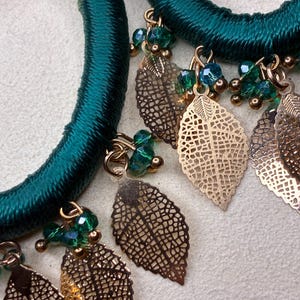 Könnte beinhalten: Nahaufnahme einer türkis-grünen Halskette mit goldenen Blattanhängern und grünen Perlenakzenten. Die Halskette hat ein dickes, seilartiges Design. Die goldenen Blattanhänger sind aufwendig detailliert.