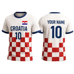 K&ouml;nnte beinhalten: Wei&szlig;es Kroatien-Fu&szlig;balltrikot mit rot-wei&szlig;em Karomuster auf der unteren Vorderseite. Das Trikot zeigt die kroatische Flagge, das Wort "CROATIA" und die Nummer "10" in Blau. Auf der R&uuml;ckseite steht "YOUR NAME" und die Nummer "10".