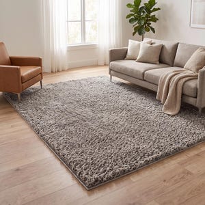 May include: A rectangular area rug with a thick, shaggy, high-pile texture in a solid medium grey colour. The rug features a dense, tufted surface with visible individual yarn loops, covering a large portion of the light-coloured wooden floor.
