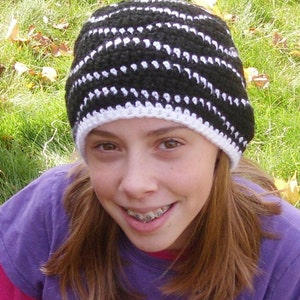 Pode incluir: Um gorro de crochê listrado em preto e branco com uma aba branca. O chapéu é feito de um fio macio e é adequado para o clima frio. O chapéu é usado por uma pessoa.