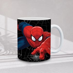 May include: White ceramic mug featuring a vibrant illustration of Spider-Man in his iconic red and blue suit. The superhero is depicted against a black background with white spiderwebs. The mug has a white handle.